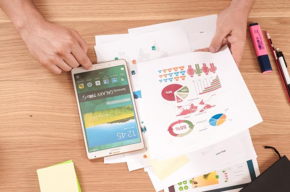 Hände über Papieren mit Diagrammen neben einem Handy
