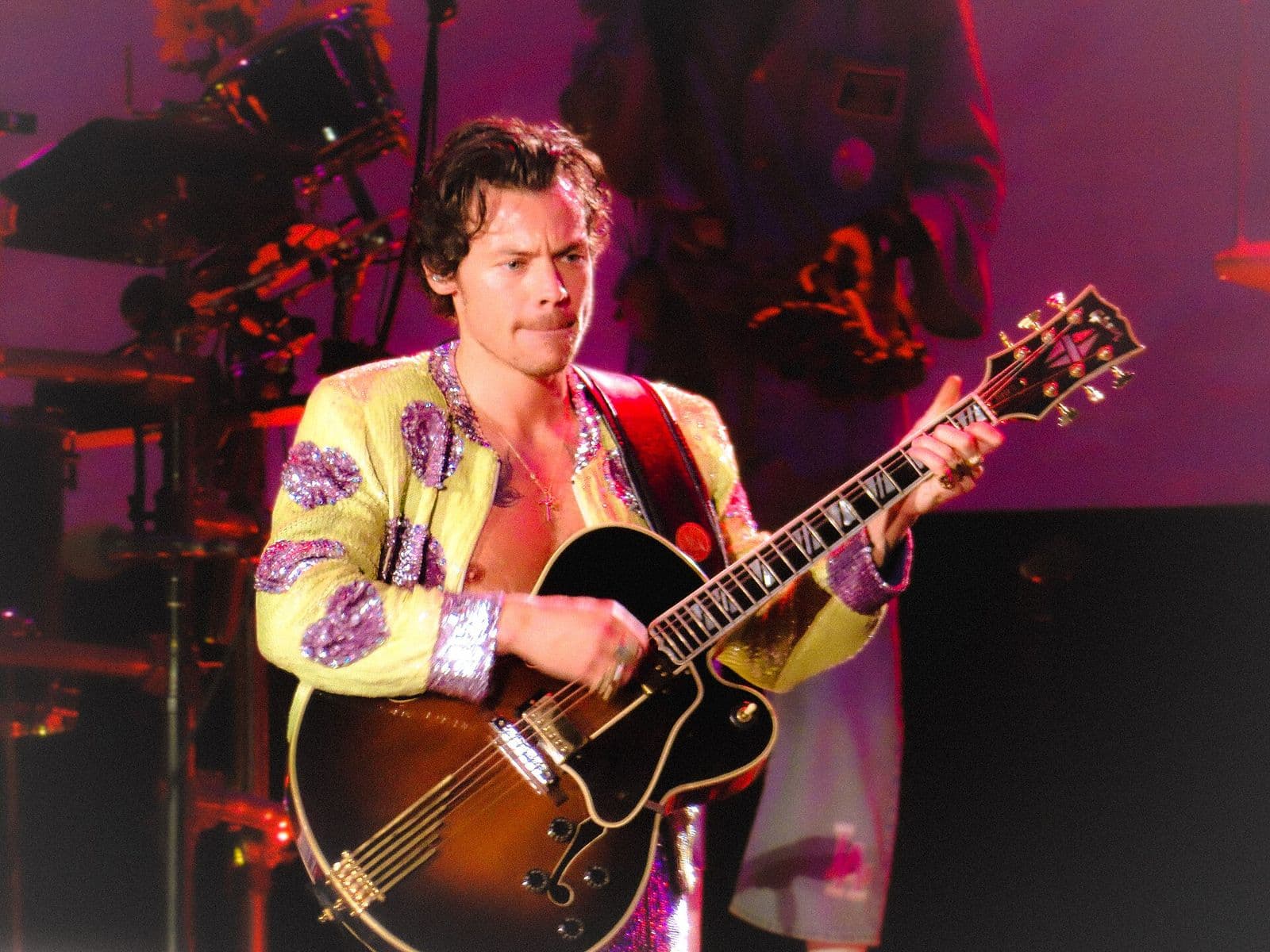 Harry Styles tocando guitarra no palco, de jaqueta verde-clara com bordados roxos, em show no Rio de Janeiro em 2022