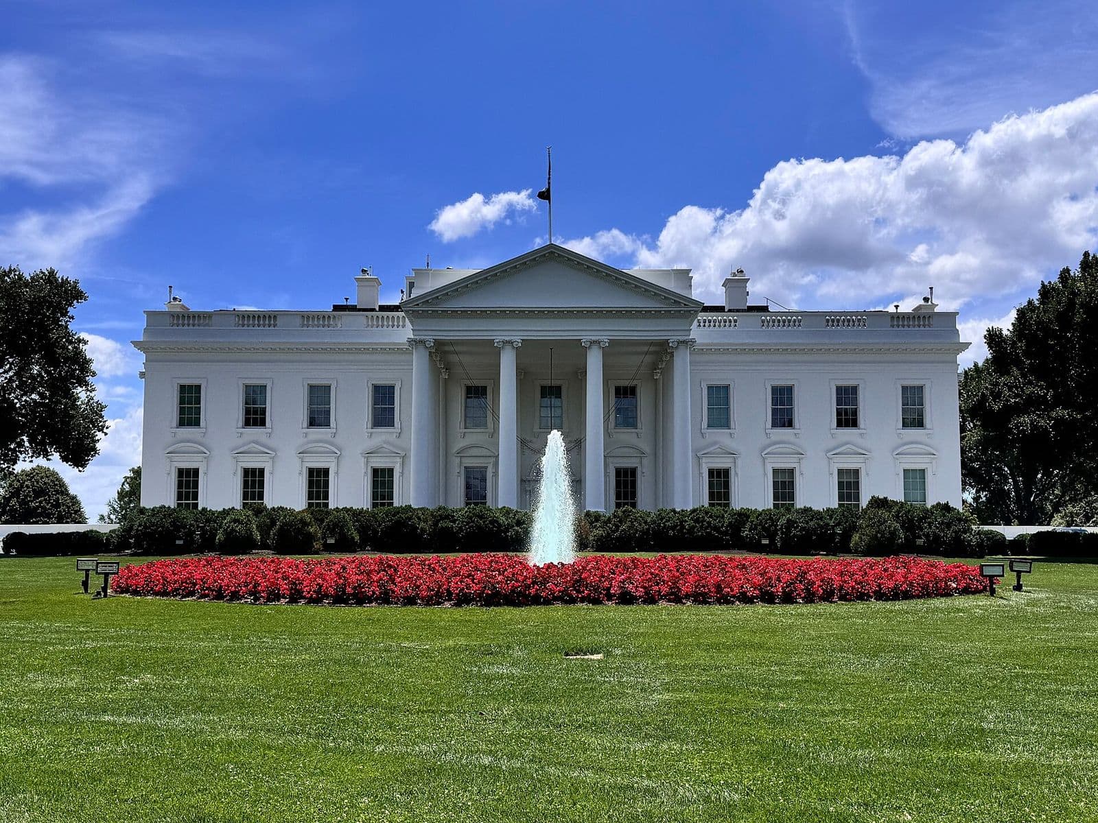 North facade of the White House in Washington, with a fountain and a bed of red flowers on the lawn, in a 2024 photo