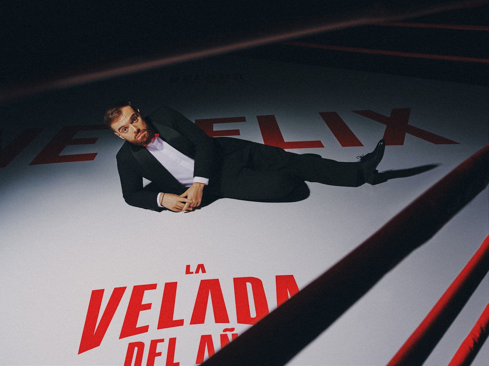 Ibai Llanos, in a tuxedo, lying on a boxing ring floor painted with the Netflix logo and the words La Velada del Año in red